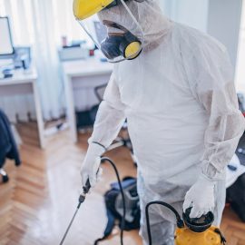 One man, man in protective suit disinfecting office work space alone.